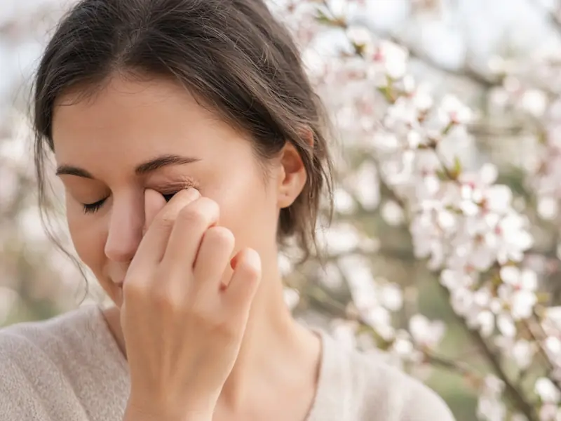 Femme qui se frotte l’œil au printemps devant un arbre en fleurs